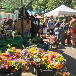 outdoor farmers' market in summer with stalls and colourful flower bunches in foreground