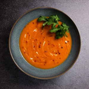 Orange soup with coriander leaf in blue bowl on grey background