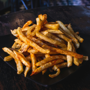 pile of fried celeriac chips - fries - on black plate against dark background