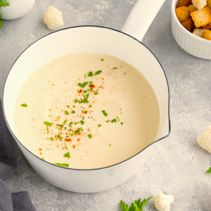 creamy soup in white bowl with chilli powder and chopped herbs on top