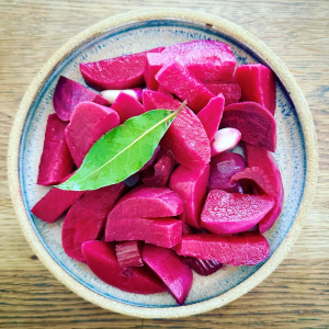 bowl of bright pink pickled vegetable wedges with bay leaf on top